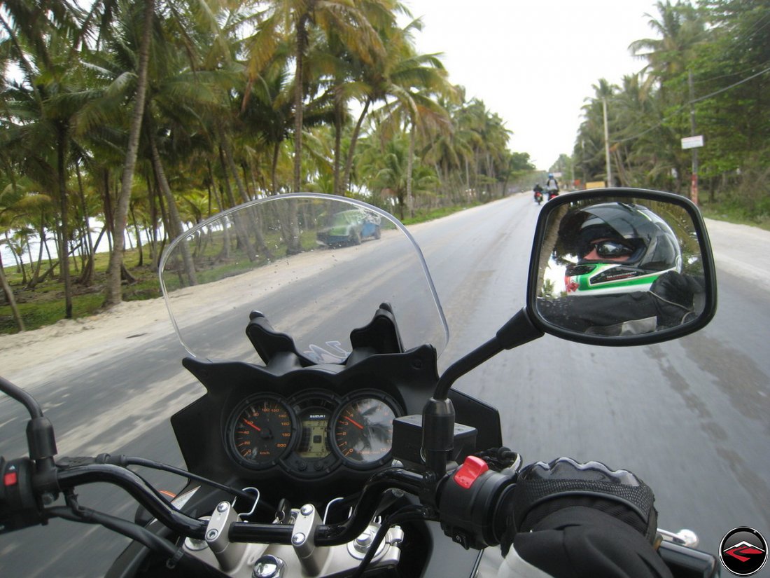 motorcycle rides down caribbean road while wind blows dust and palm trees