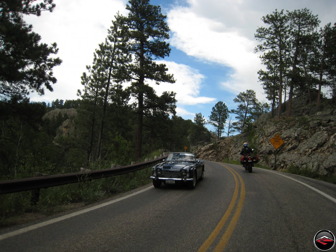 Ducati Multistrada Motorcycle passing a vintage Triumph TR3 Sports Car while riding over the Pigtail Bridges on the Norbeck Scenic Byway in South Dakota