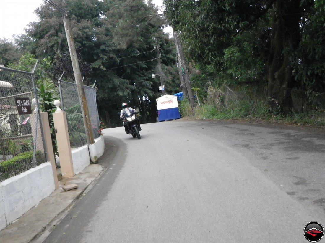 Riding a Suzuki V-Strom 650 motorcycle with steel fencing and concrete walls immediately along the shoulder of the road