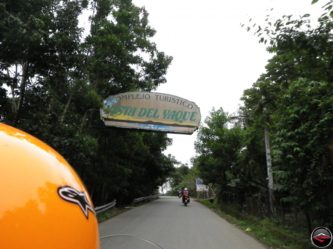 Riding motorcycles in the Dominican Republic with a sign over the top of the road that reads Complejo Turistico Vista Del Yaque