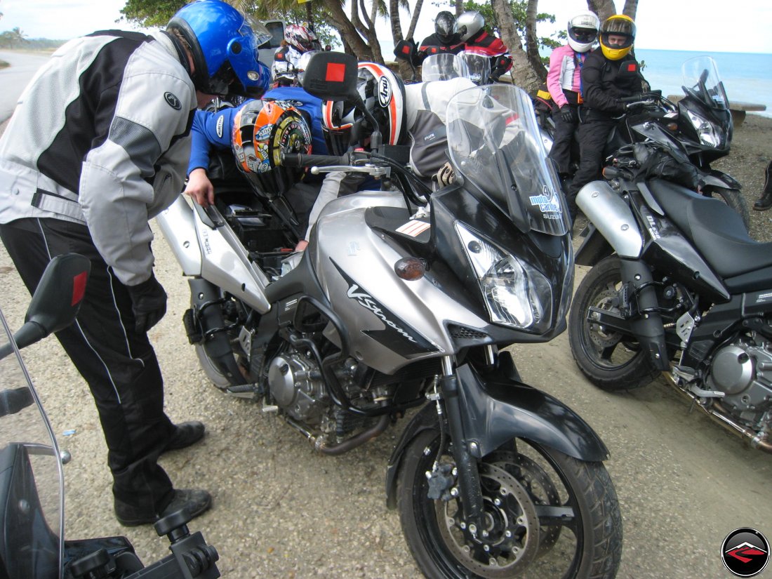 Three guys work on a loose battery connection on a Suzuki V-Strom 650 Motorcycle