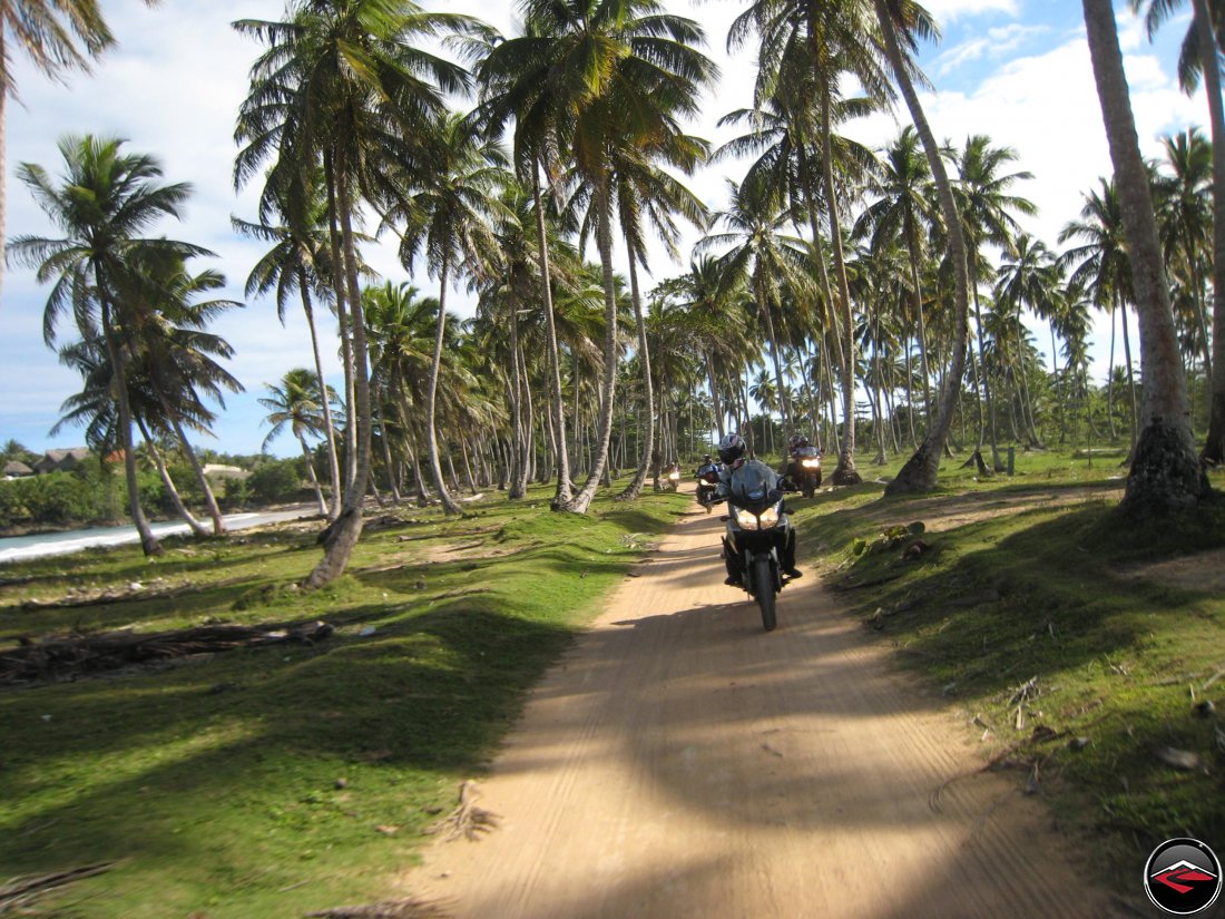 Epic motorcycle riding along a perfect sandy road following the caribbean coastline of the Dominican Republic with palm trees blowing in the wind