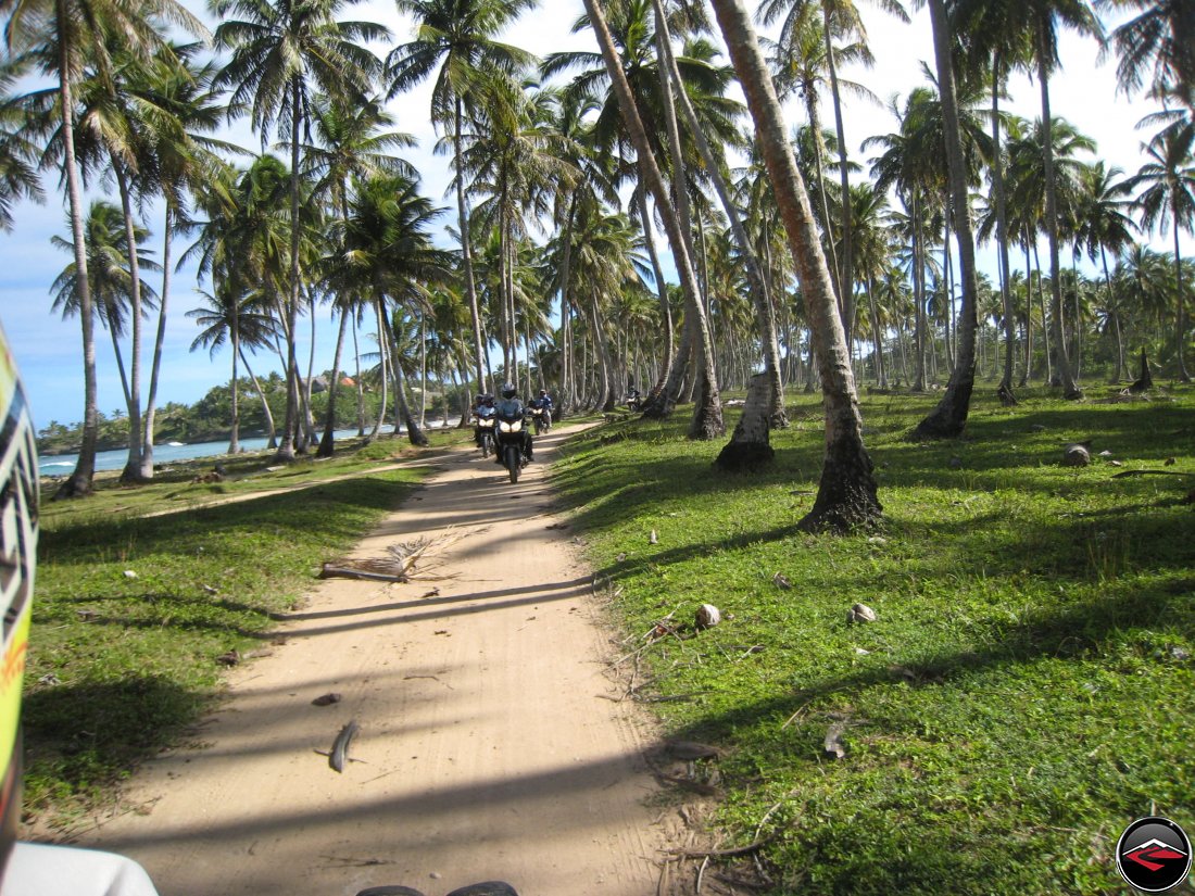 Epic motorcycle riding along a perfect sandy road following the caribbean coastline of the Dominican Republic with palm trees blowing in the wind