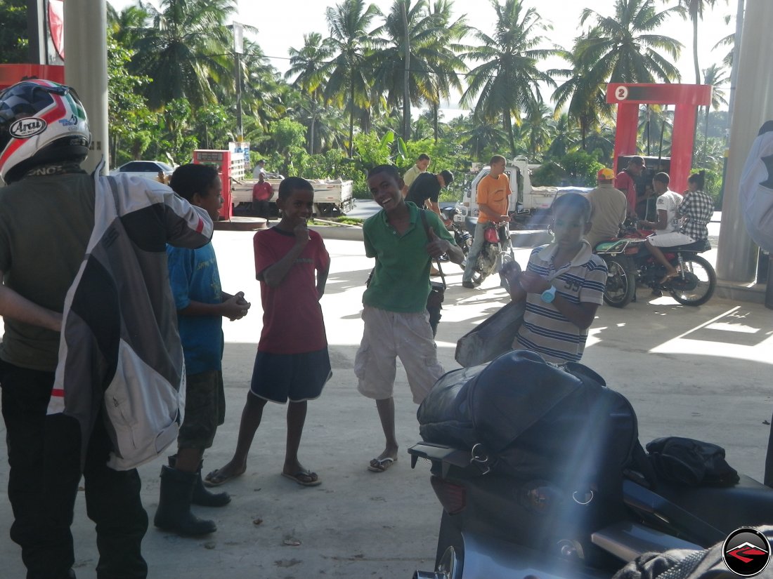 Motorcycle stopping for gas and local boys with shoe shine kits show up