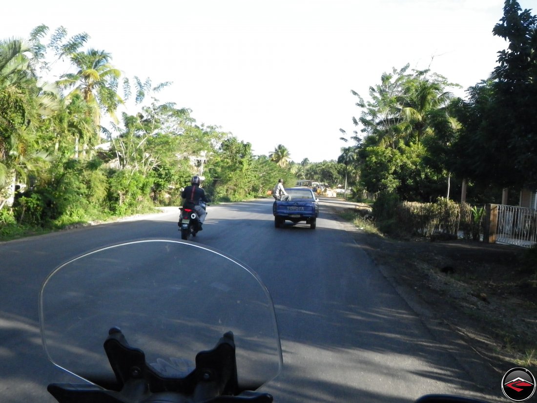 Motorcycle passing a toyota pickup ith a man sitting dangerously on the side of the pickup bed