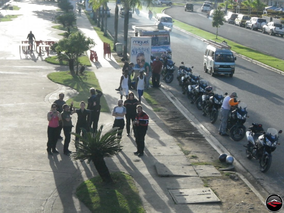 motorcycles parked along the side of the road while riders interact with locals