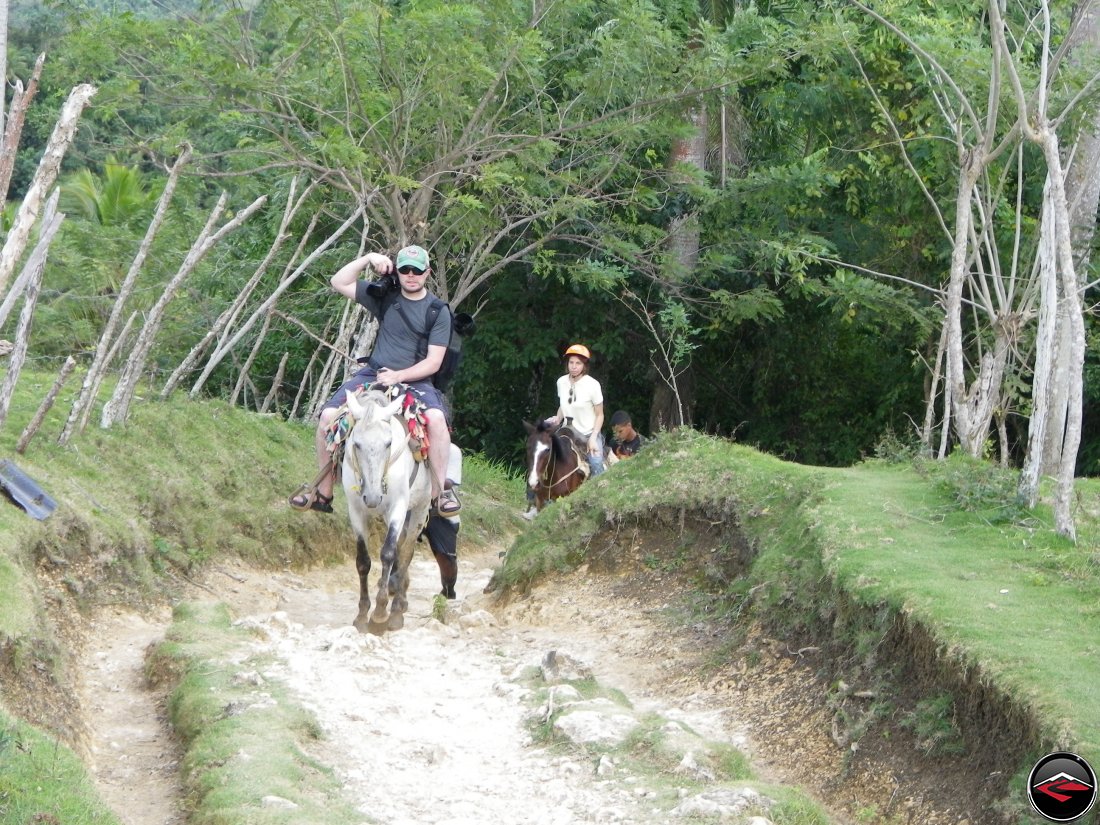 man taking photos from the back of a small white horse Cascada El Limon Dominican Republic