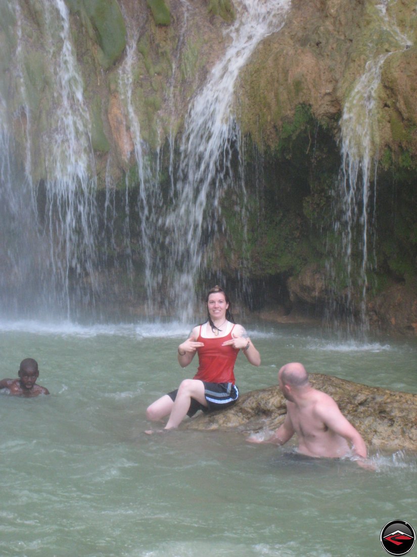 woman covering her nipples while sitting on a rock in front of a waterfall Cascada El Limon Dominican Republic