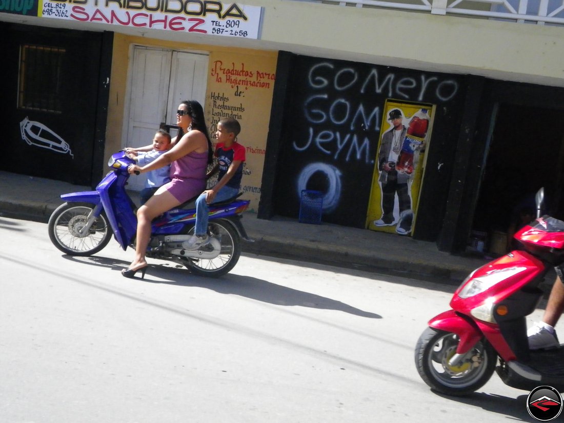 woman wearing spike high-heels riding a scooter with two children as passengers