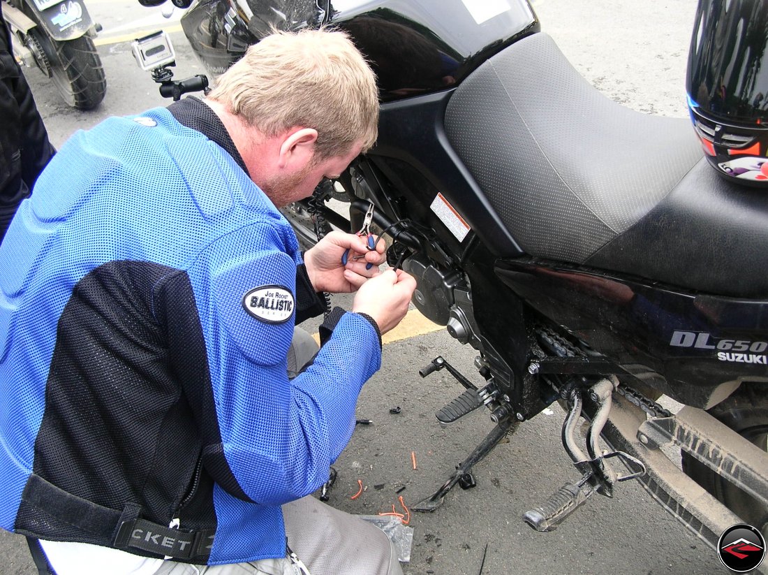 Man modifying the wiring on a Suzuki V-Strom 650 motorcycle in a parking lot