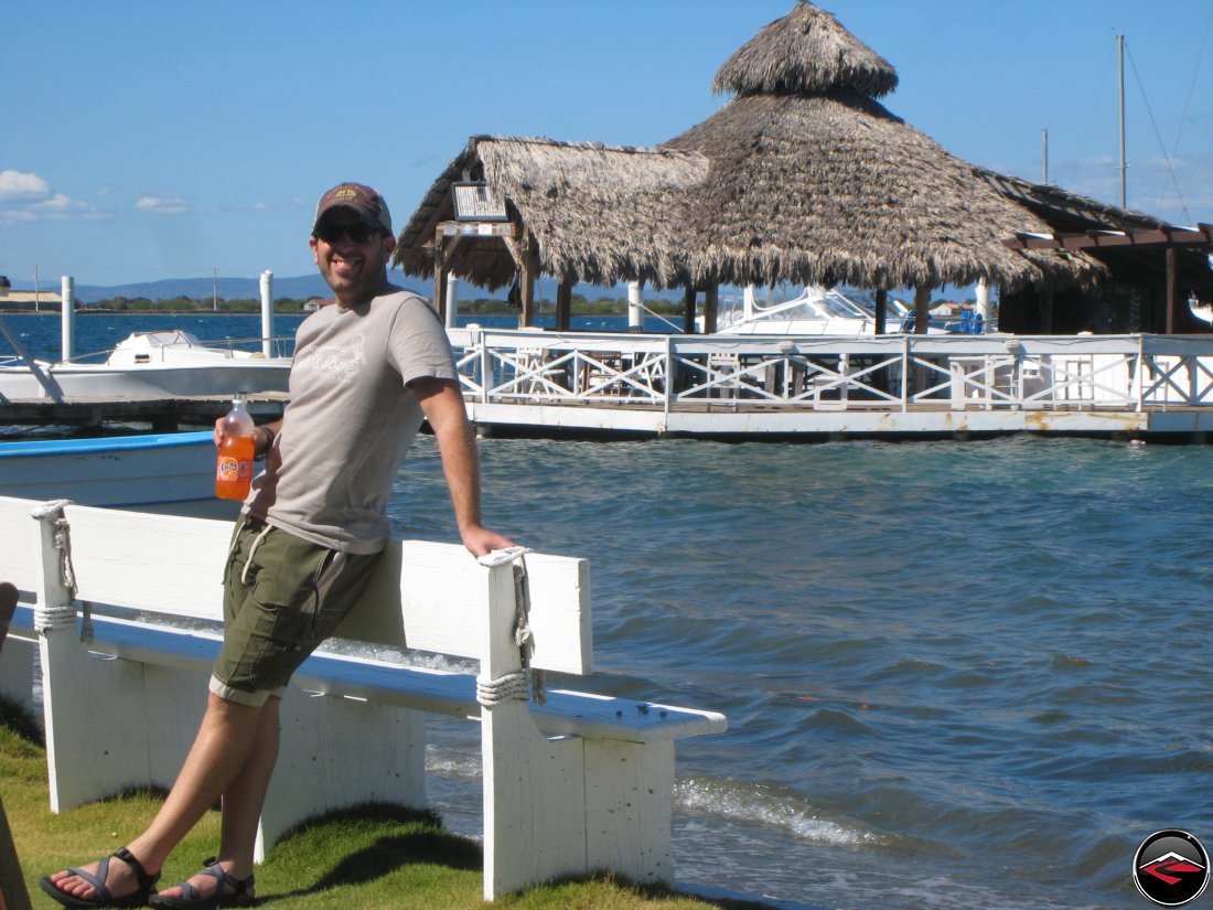 Man drinking orange fanta in front of thatched roof cabana