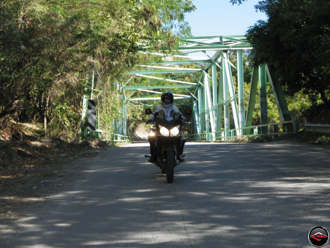woman riding a motorcycle over a steel trellis bridge