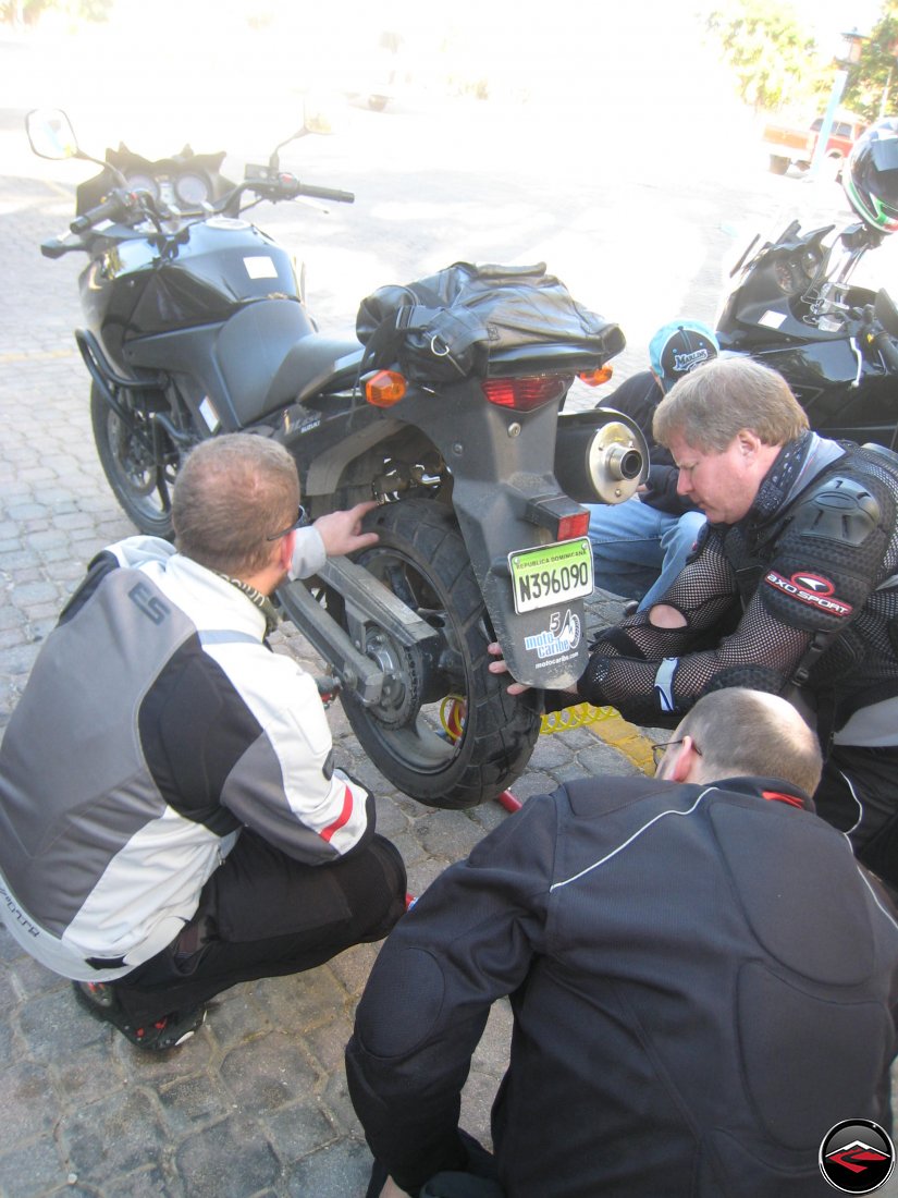 three men work on fixing a flat motorcycle tire