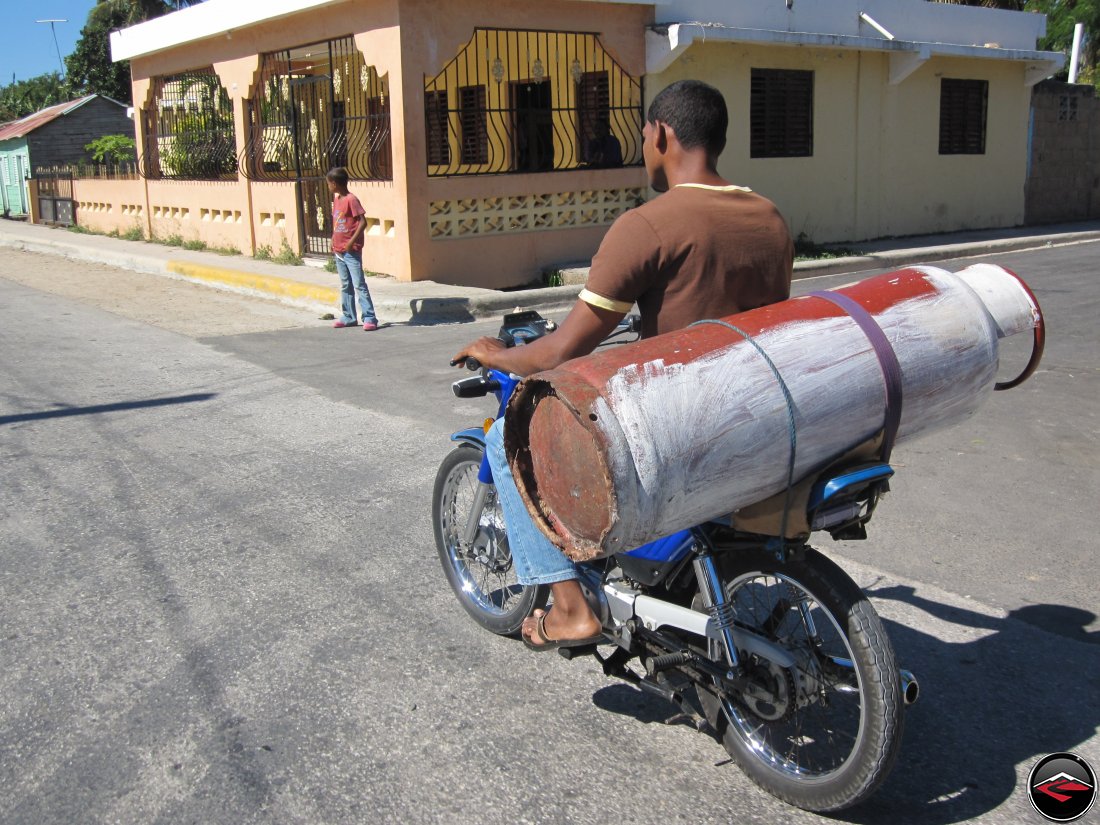 man hauling massive propane tank on motorcycle