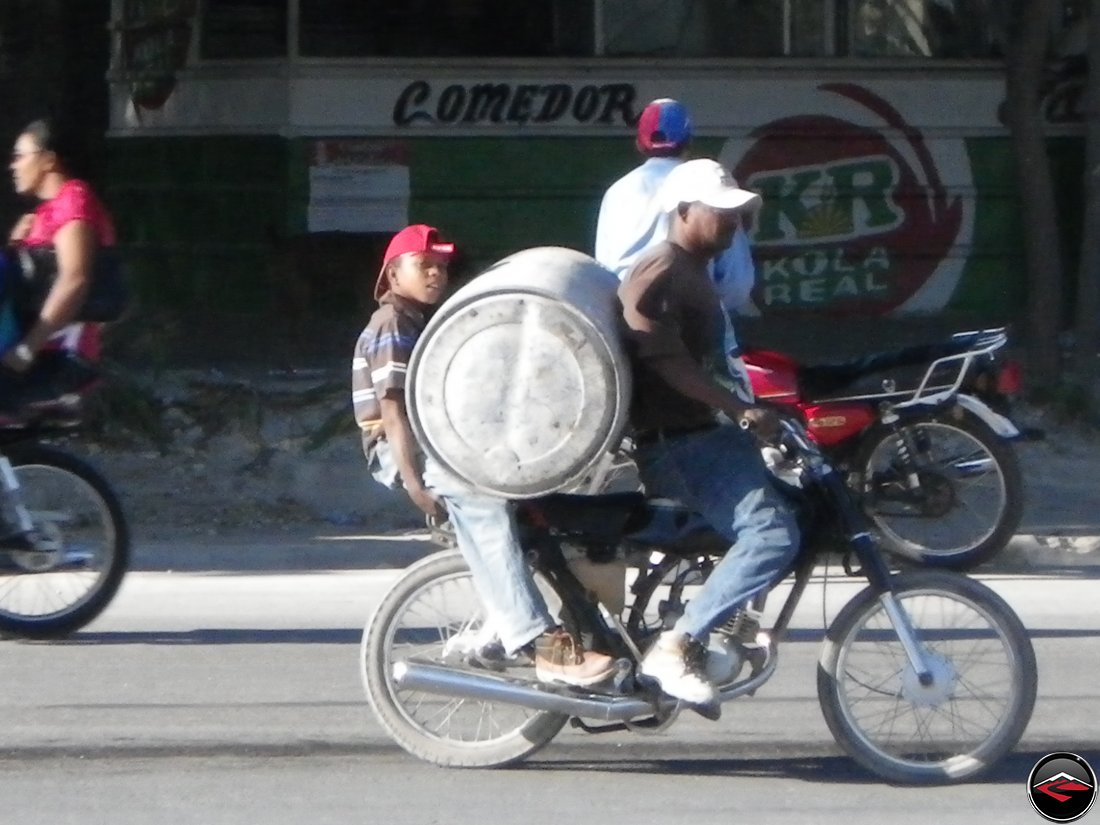 man and boy hauling massive barrel on a motorcycle