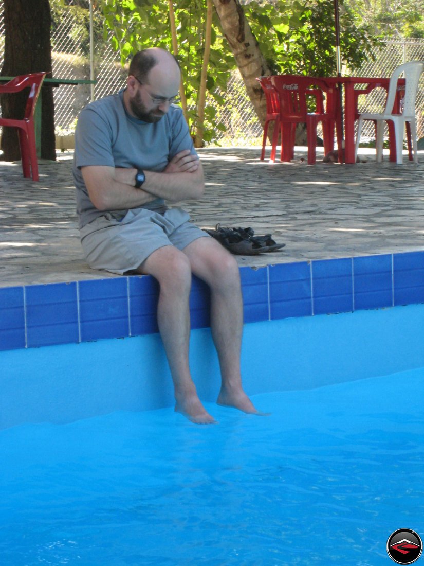 grumpy man looking miserable while soaking his feet in a pristine swimming pool