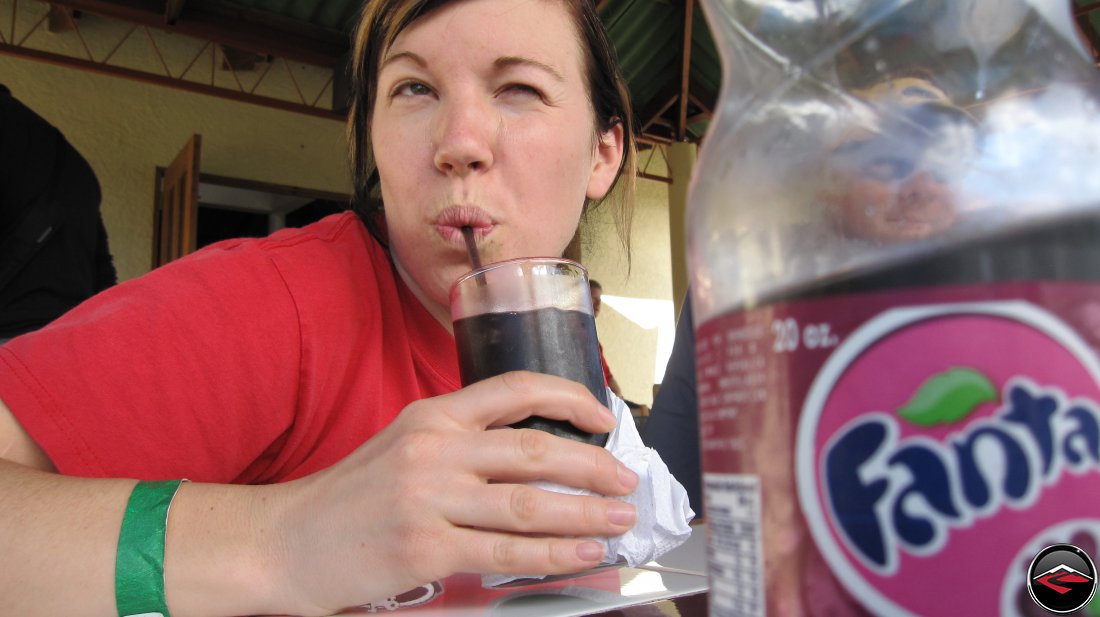 Pretty girl making a funny face while drinking grape fanta soda through a straw