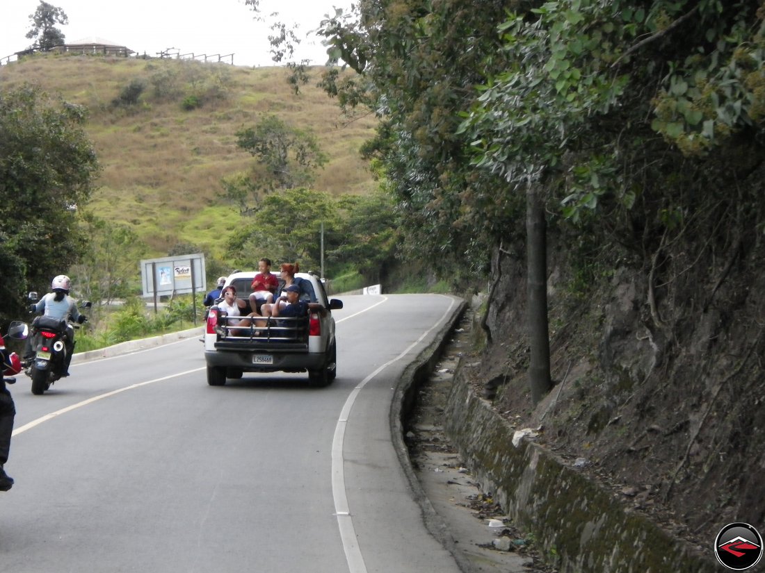 girl on a motorcycle passing a pickup truck full of people