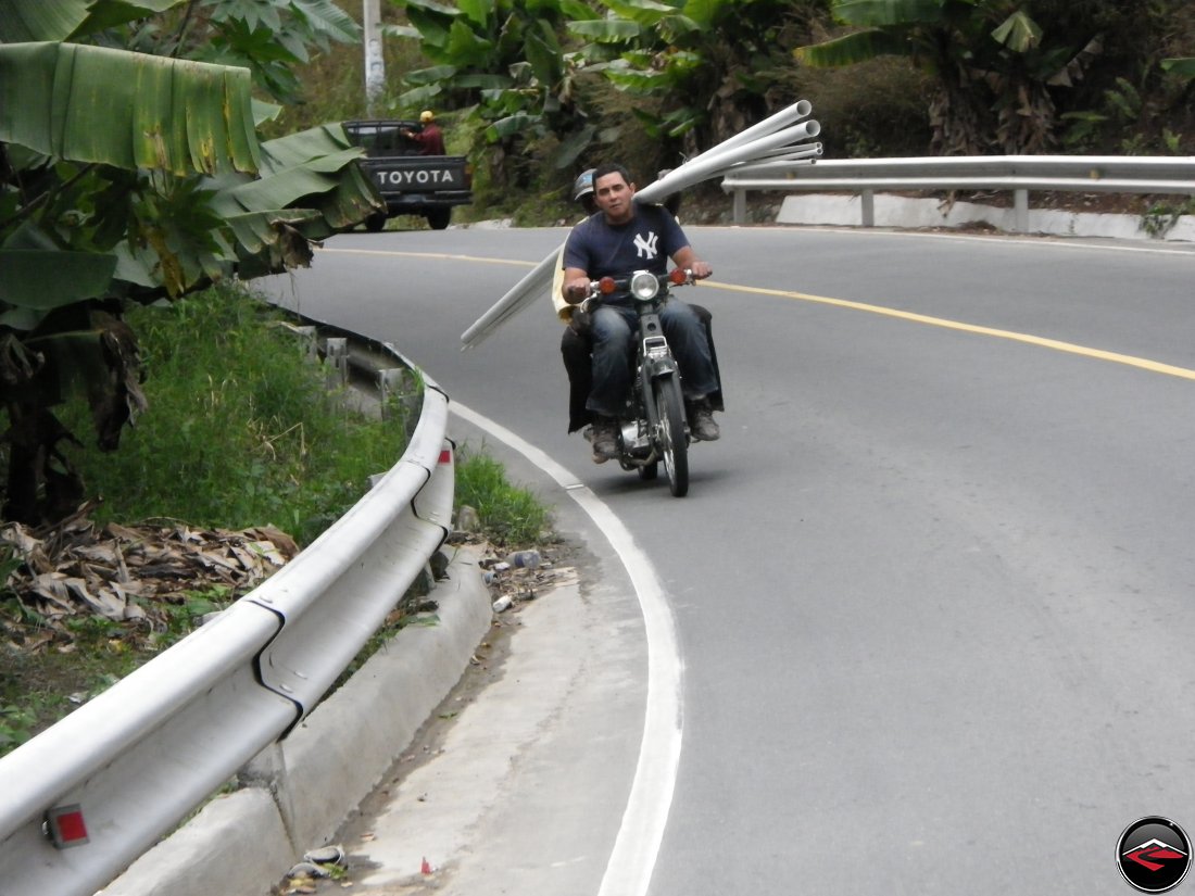Two men on a motorcycle carrying long PVC pipe