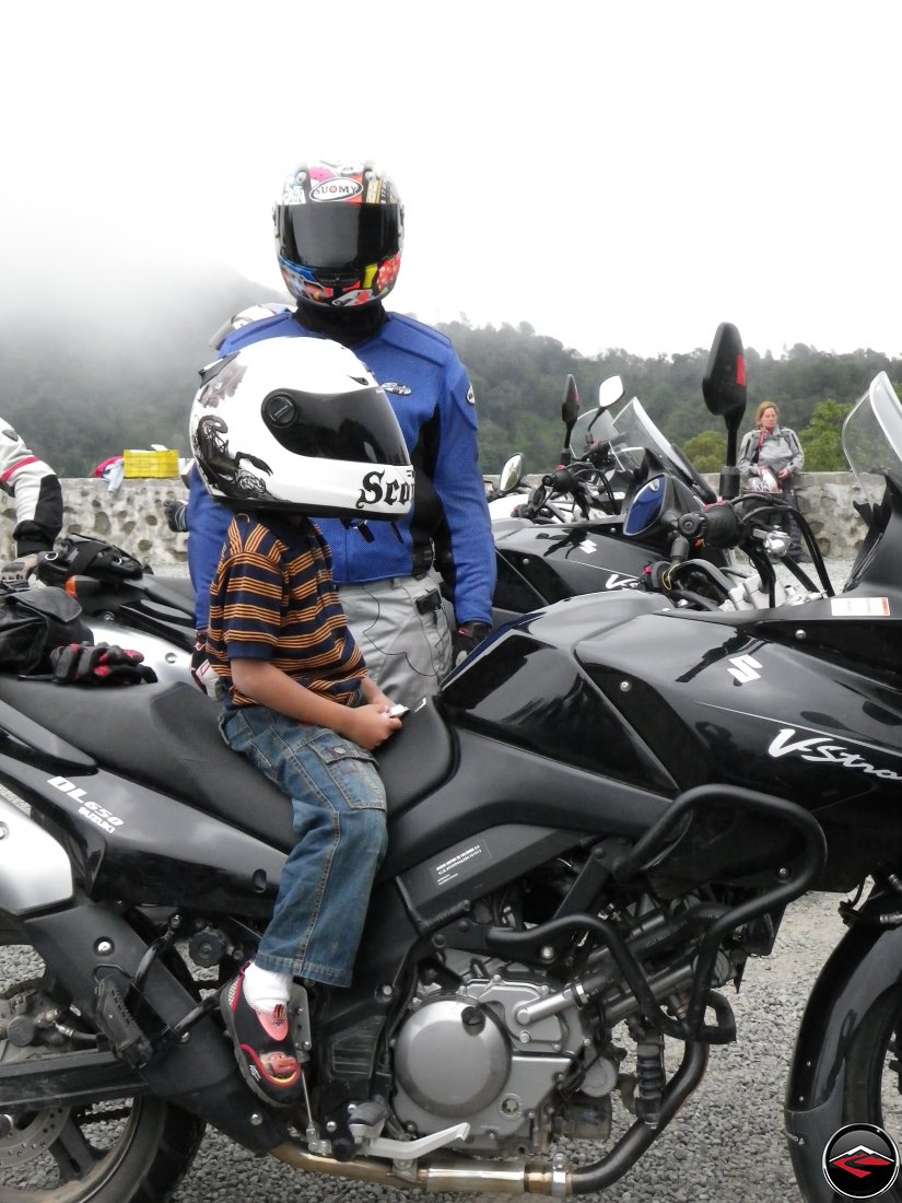 Man in a suomy helmet with a young boy sitting on a motorcycle wearing a scorpion helmet