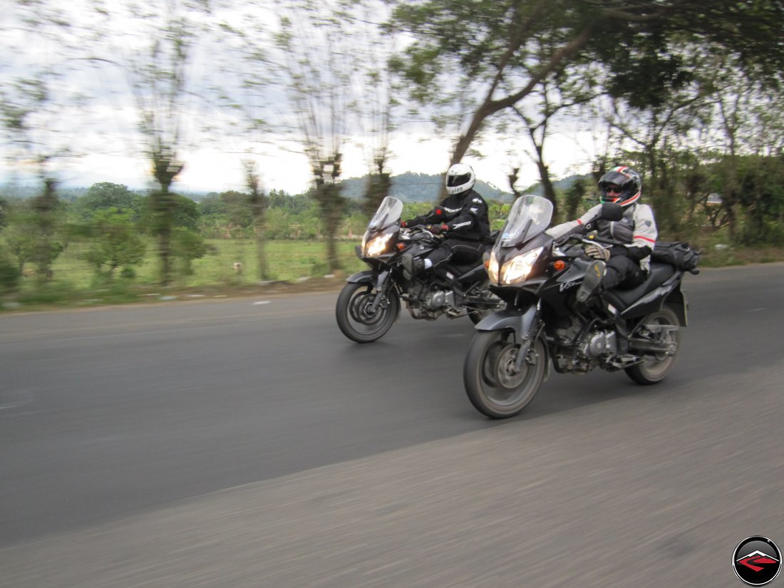 Two men riding matching motorcycles side by side down a highway