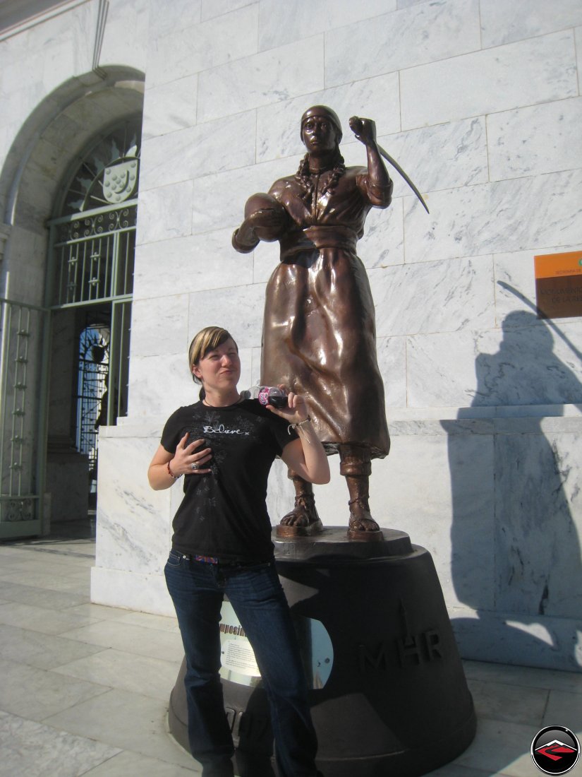 Girl mimicking copying the statue behind her groping her own breast