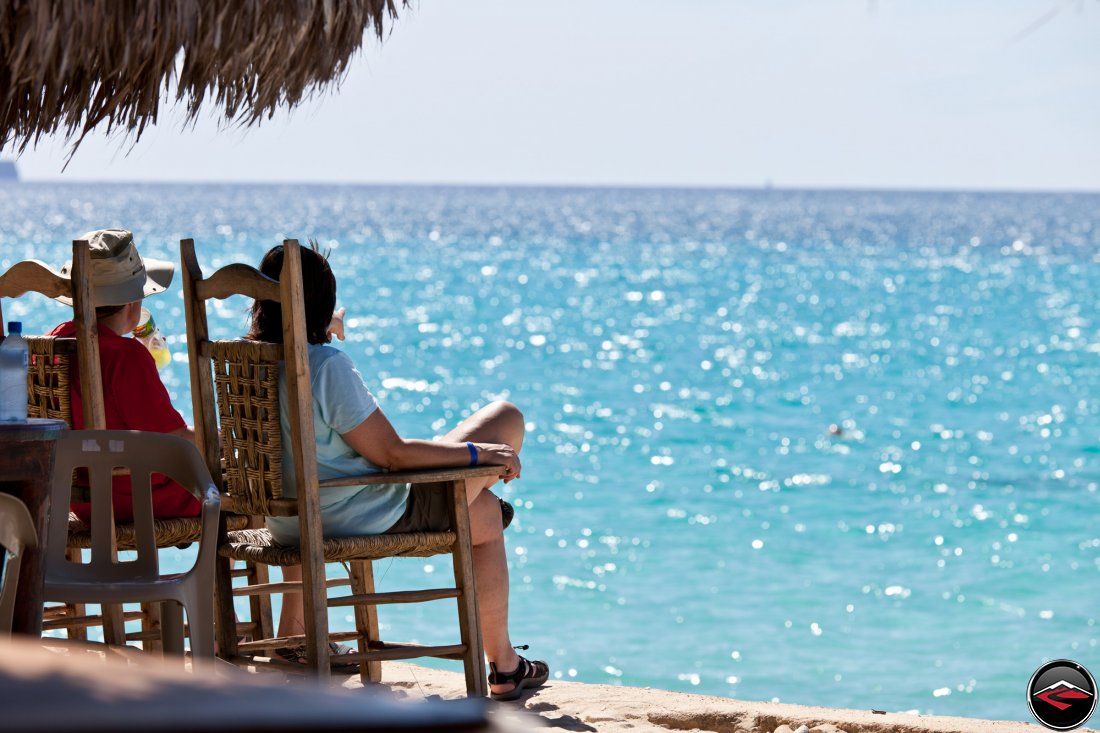 Man and woman sitting on a caribbean beach pointing out at the perfect water