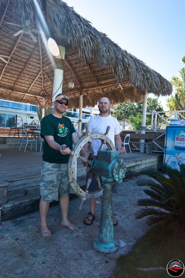 two men playing with a ships steering wheel