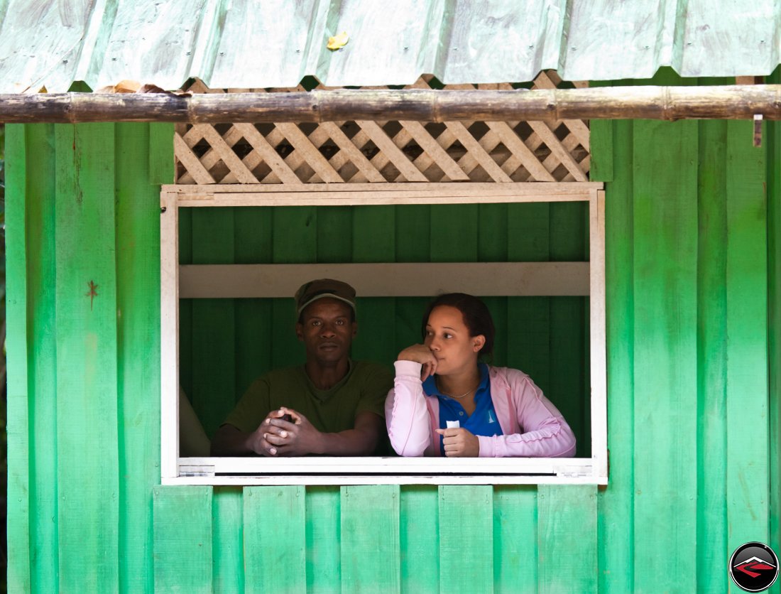 Man and woman look out the window of a green shack in the dominican republic on a caribbean island