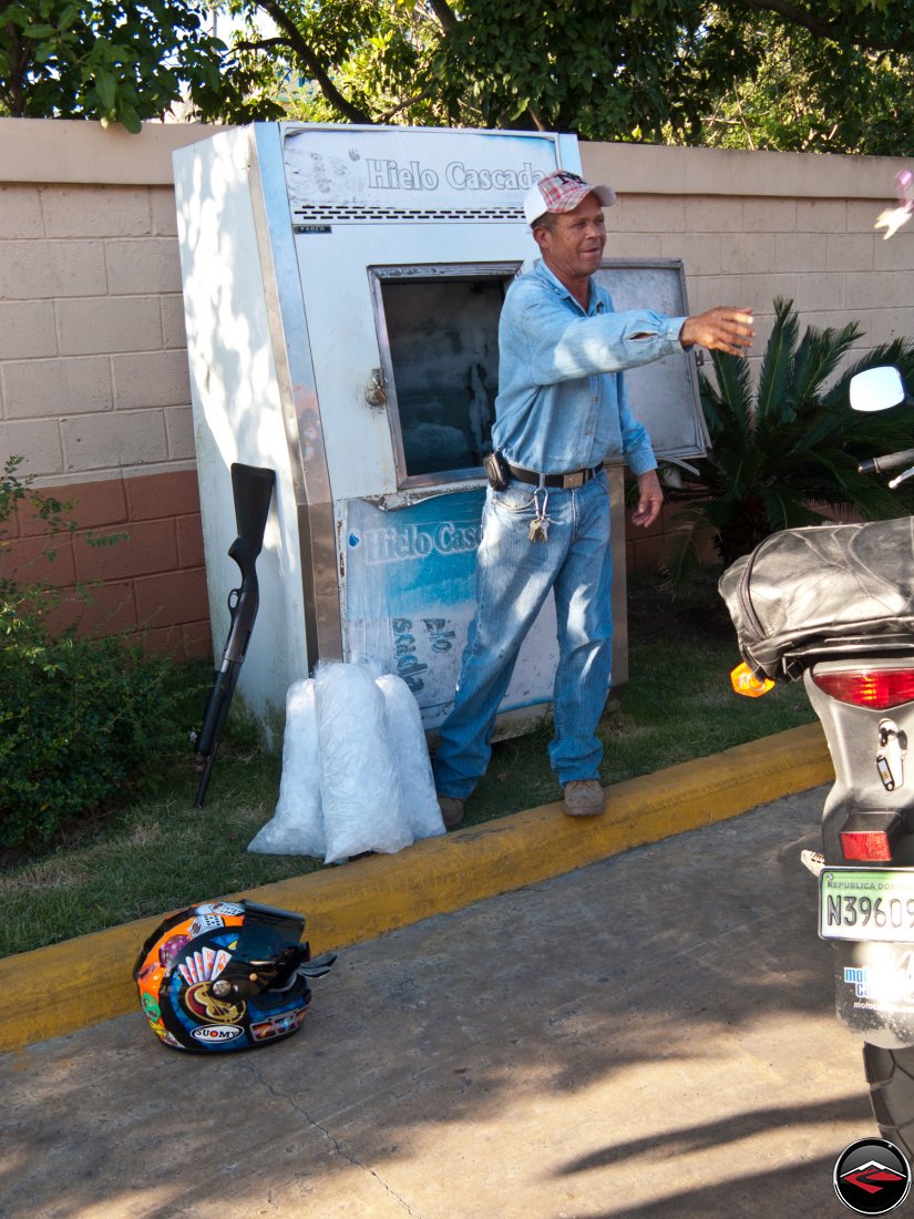 dominican republic gas station guard leans his shotgun against the wall to sell ice