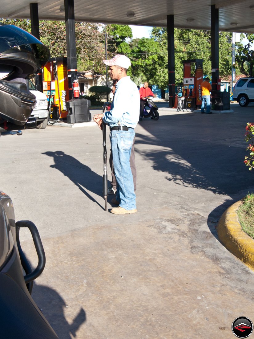 local dominican republic guarding a gas station with a shotgun