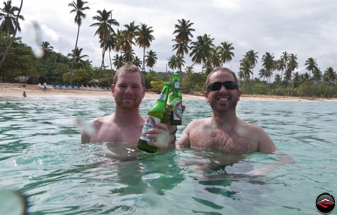 Two men drinking presidente beer while standing in caribbean ocean water Playa Rincon Dominican Republic