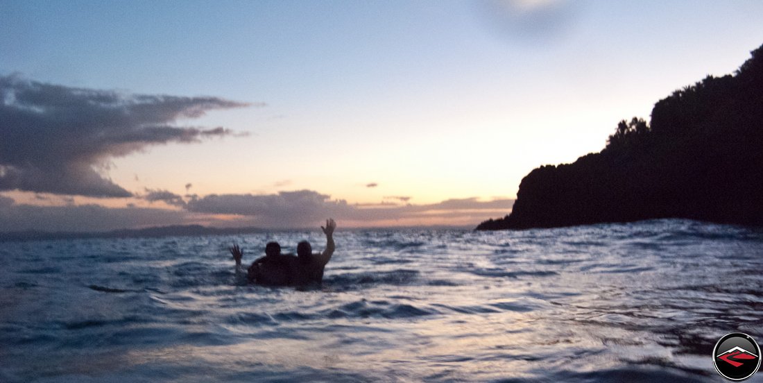 silhouette of two men in the ocean waving to the camera at sunset La Tambora Beach Resort