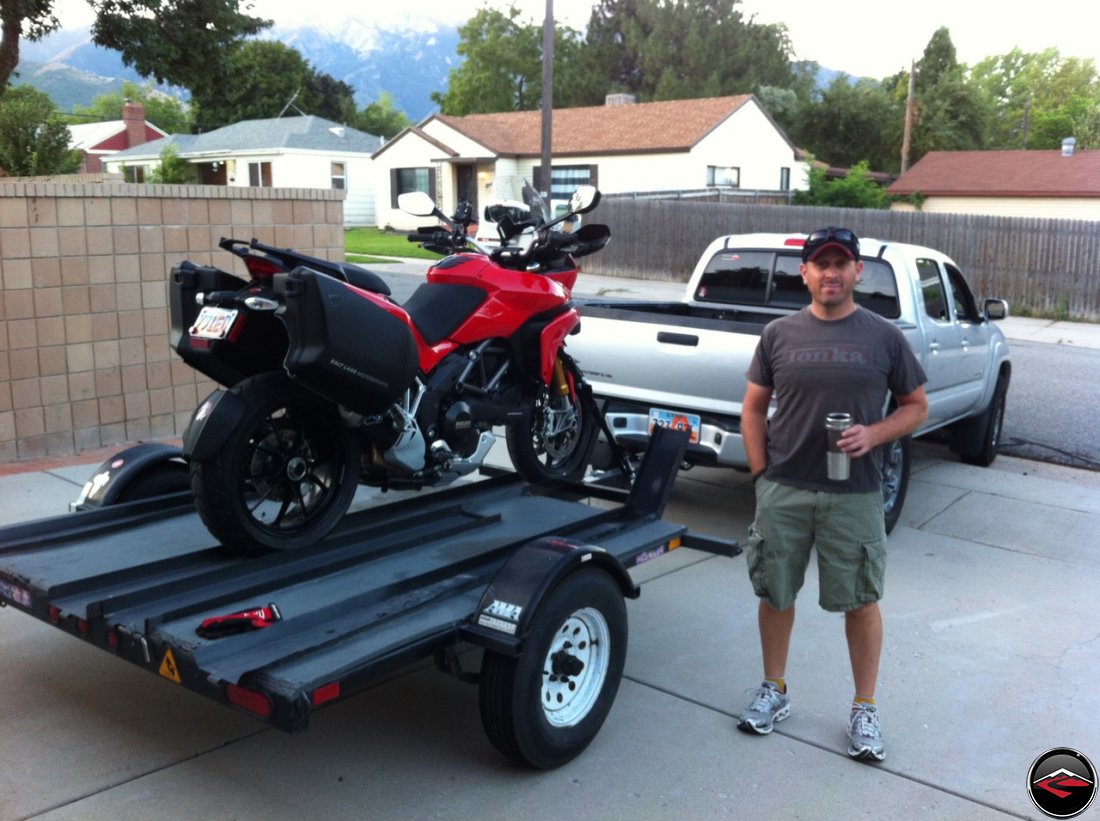 Dave drinking a cup of coffee, standing next to a Ducati Multistrada 1200 loaded on a 3-rail trailer attached to a Toyota Tacoma