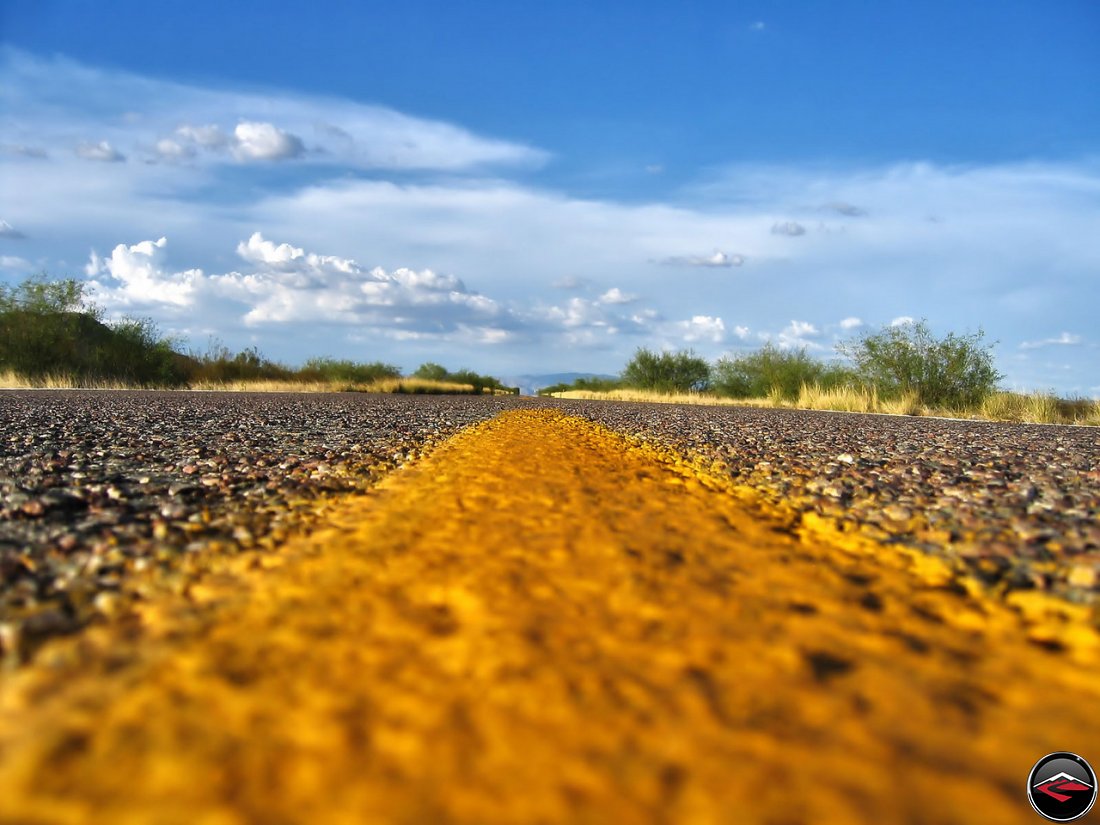 Yellow lines in the center of an Empty California Road, with scattered clouds in the distance