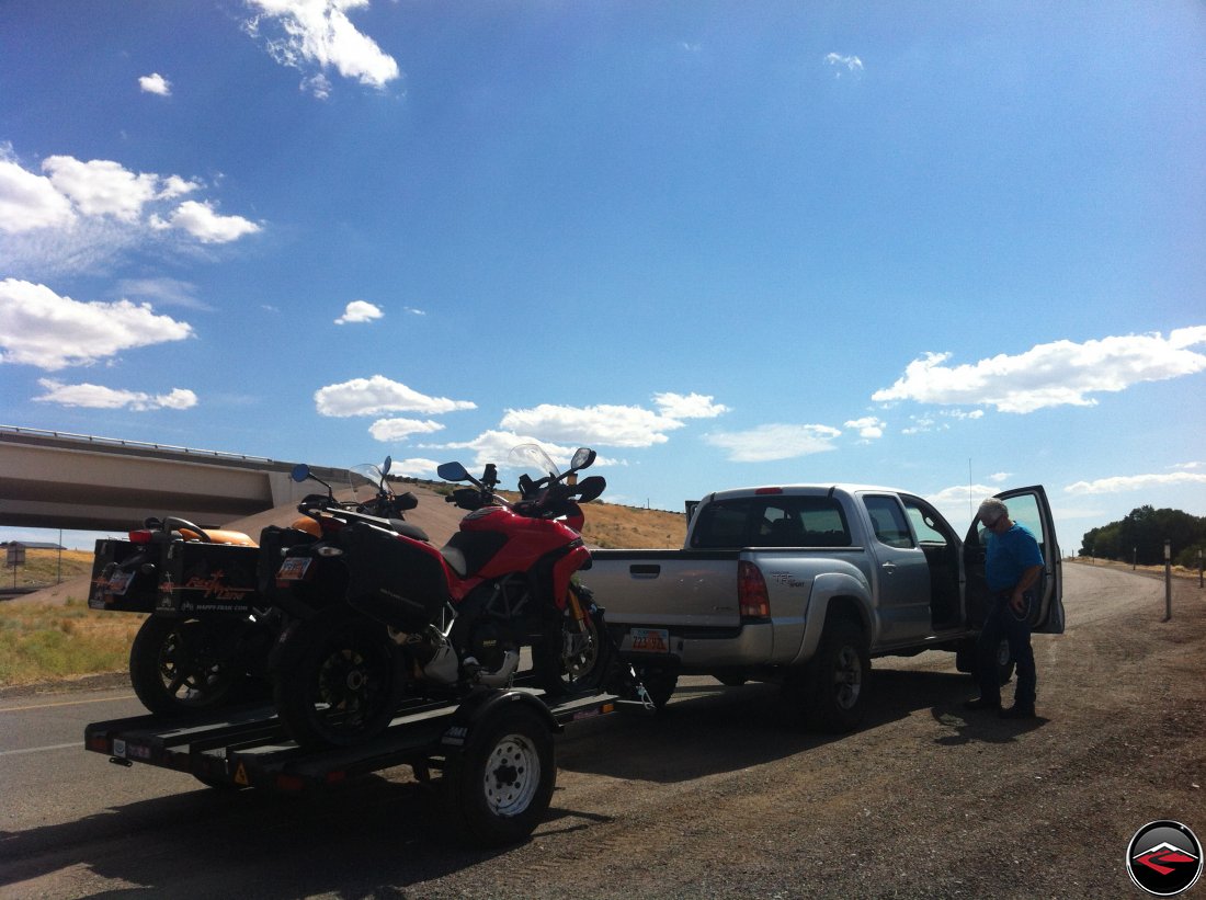 Checking tire pressure on a Toyota Tacoma and checking tie down straps on a Ducati Multistrada 1200 and a Buell Ulysses while tied down to a 3-rail motorcycle trailer