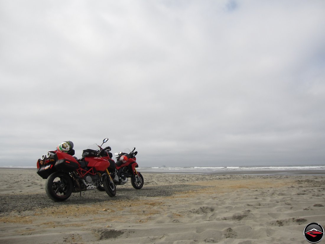 Two Red Ducati Mulstistrada S motorcycles parked ont he beach looking over the Pacific Ocean